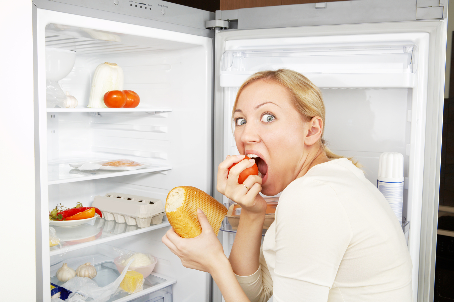 The woman greedy eats meal against an open refrigerator